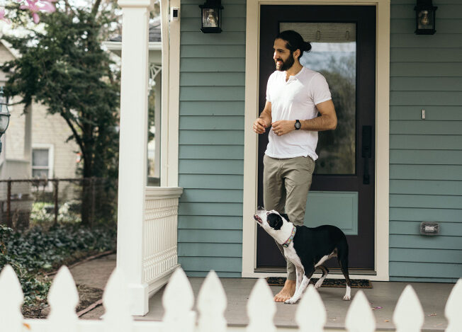 A man and his dog on the front porch of their blue house celebrate homeownership.