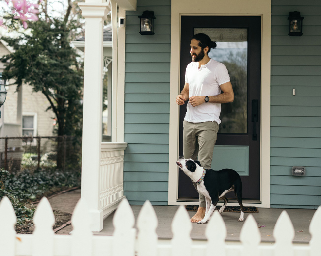A man and his dog on the front porch of their blue house celebrate homeownership.