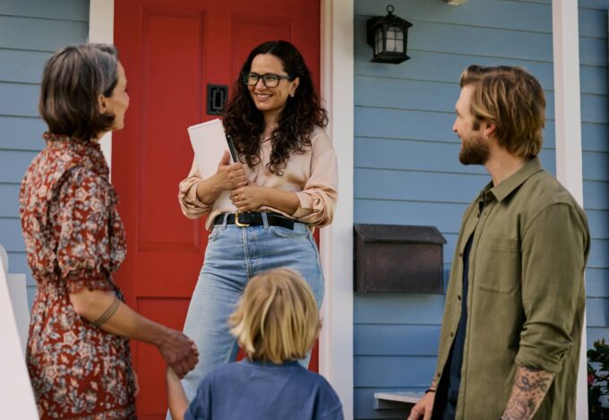 Realtor meets with a first-time homebuyer family outside of blue home for sale.