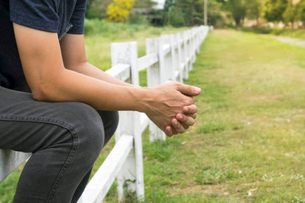 Someone sitting on a fence in a field. They are holding their hands together.