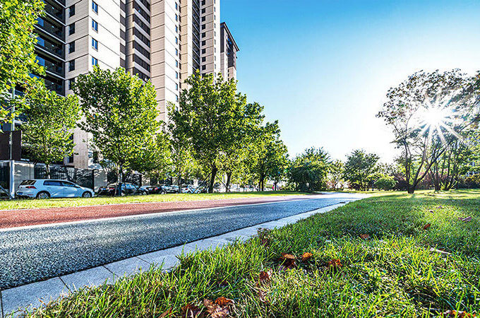 Street view of a residential building with the sun shining through the trees. Lighting the street and the grass by the building.