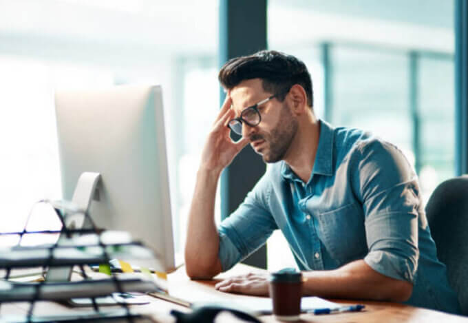 A man with glasses sitting at an office desk. Looking at the computer screen with a concerned expression