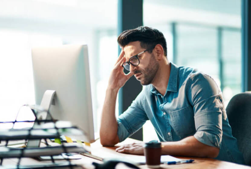 A man with glasses sitting at an office desk. Looking at the computer screen with a concerned expression