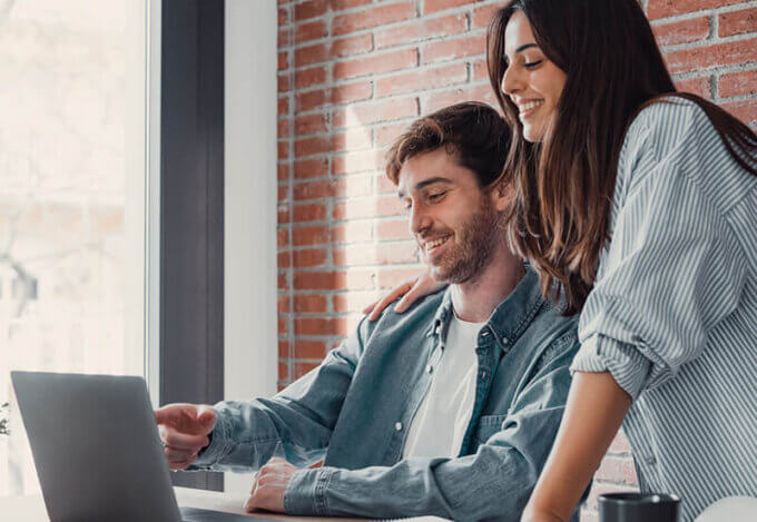 Smiling couple looks at a laptop together while planning how to buy a house, reviewing finances and mortgage options.