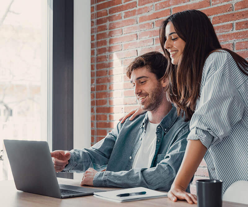 Smiling couple looks at a laptop together while planning how to buy a house, reviewing finances and mortgage options.