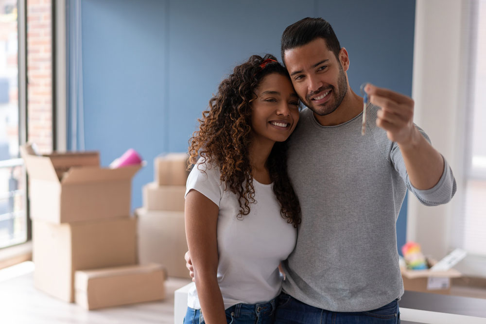 New homeowners looking at the keys to their home. Moving boxes in the background.