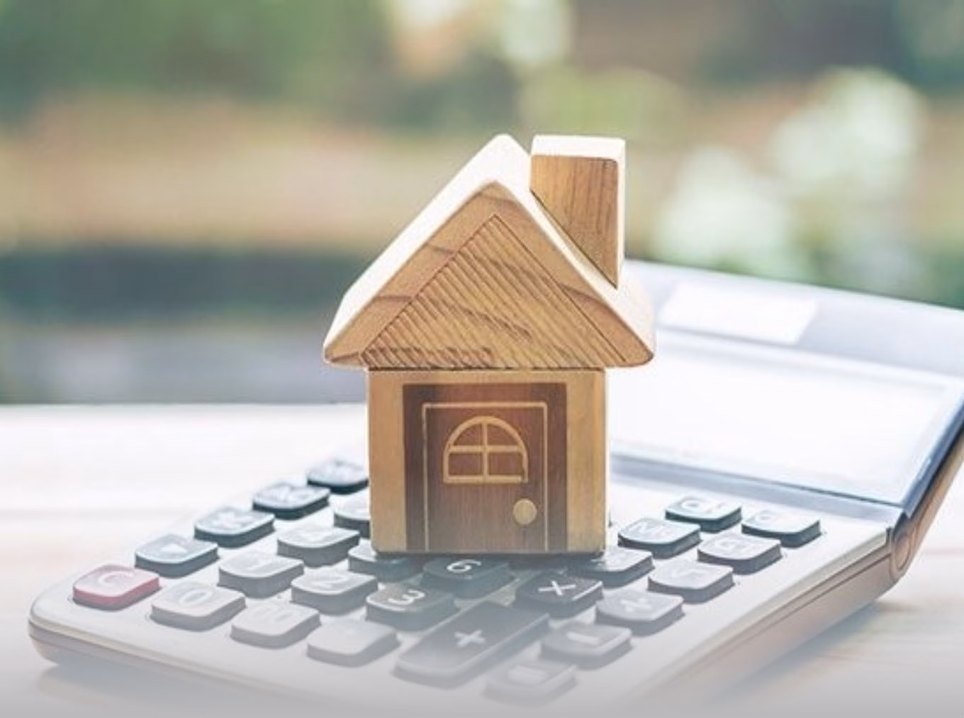 A wooden toy house on a desk calculator.