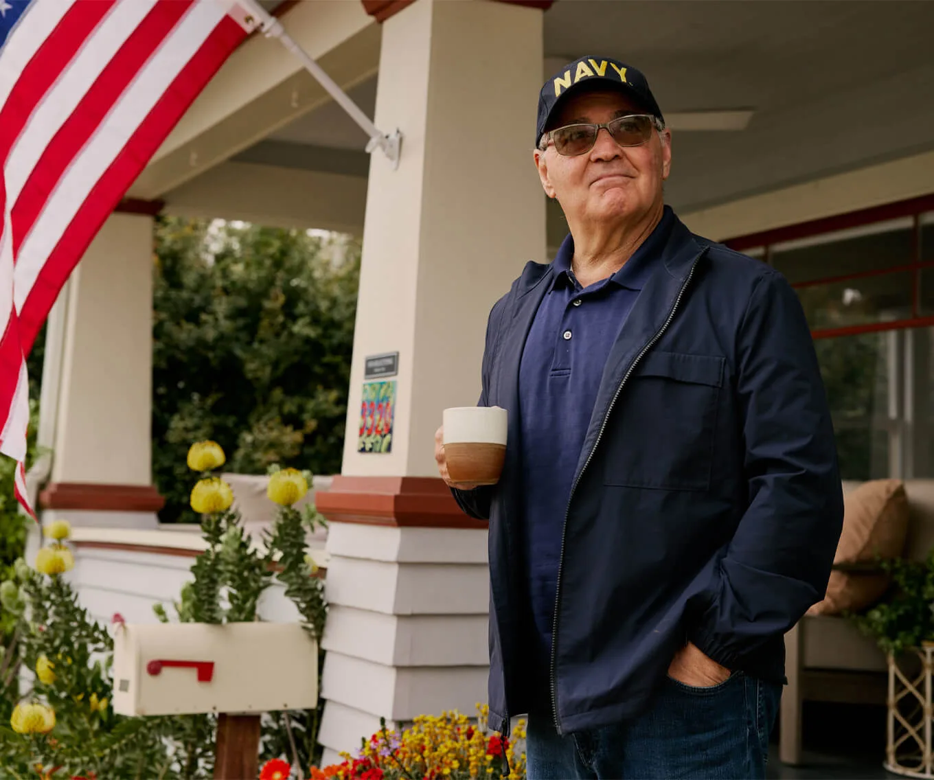 Navy veteran homeowner standing on his front porch with an American flag and mailbox, representing property tax savings through a homestead exemption.