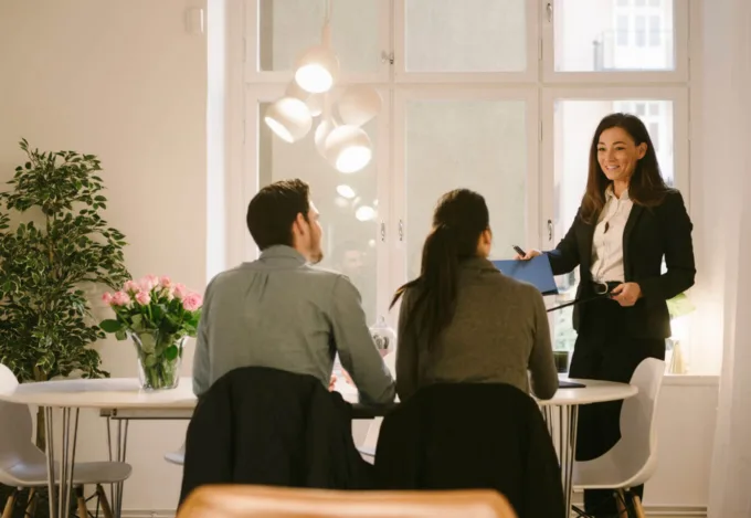 Professional woman reviewing paperwork with a couple at a table during a real estate closing or title insurance meeting.