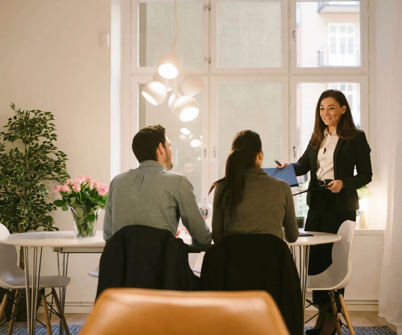 Professional woman reviewing paperwork with a couple at a table during a real estate closing or title insurance meeting.