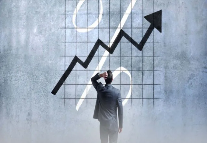 A man in a suit scratching his head. Looking at a large graph on a wall.