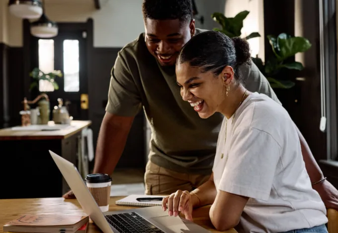 Couple smiling while reviewing finances on a laptop at home, exploring ways to lower their mortgage payment and manage monthly housing costs