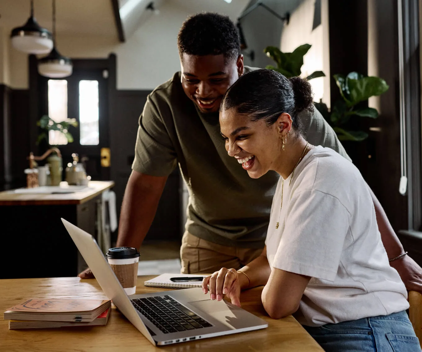 Couple smiling while reviewing finances on a laptop at home, exploring ways to lower their mortgage payment and manage monthly housing costs