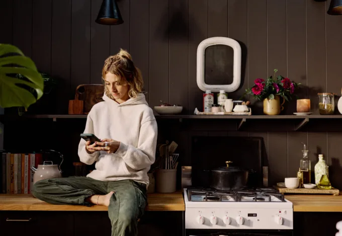 Homebuyer sitting in a modern kitchen reviewing information on a phone, representing key questions to ask when buying a house and preparing for the homebuying process