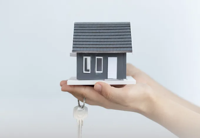 Hands holding a small model home and a key