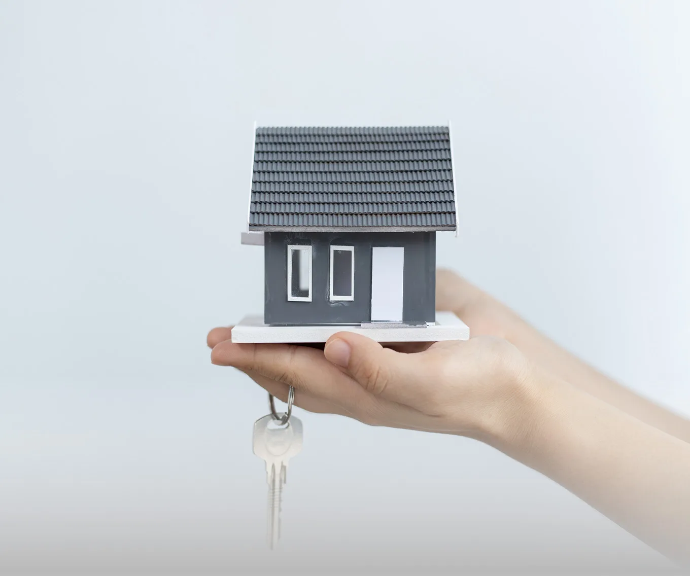 Hands holding a small model home and a key