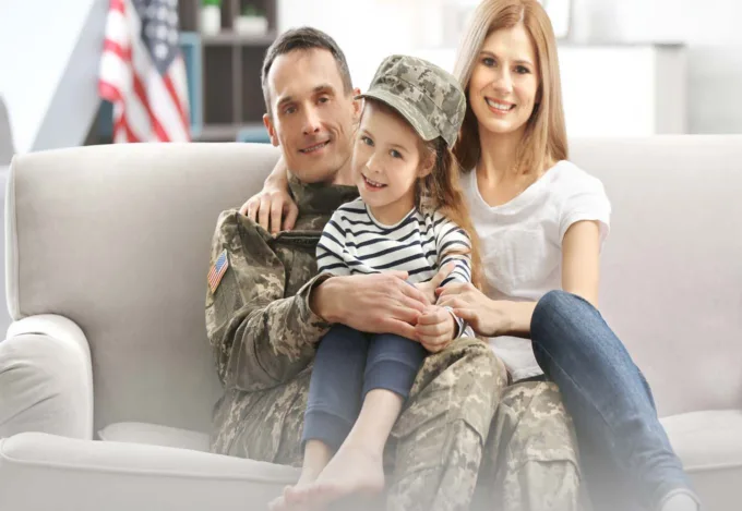 A Veteran sitting on the couch with his family. In their home they got with a VA loan
