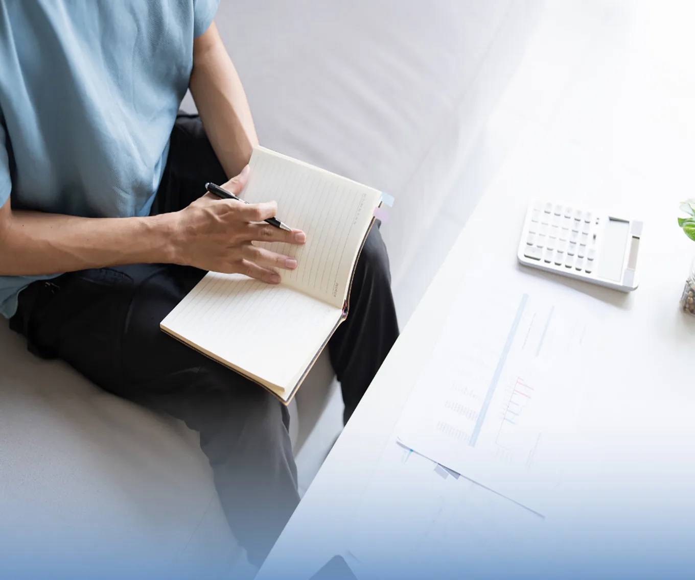 A potential homebuyer sitting on their couch, holding an open notebook. A calculator on the coffee table in front of them.