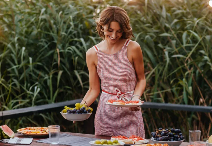 Woman preparing snacks for hosting a home outdoor gathering with string lights.