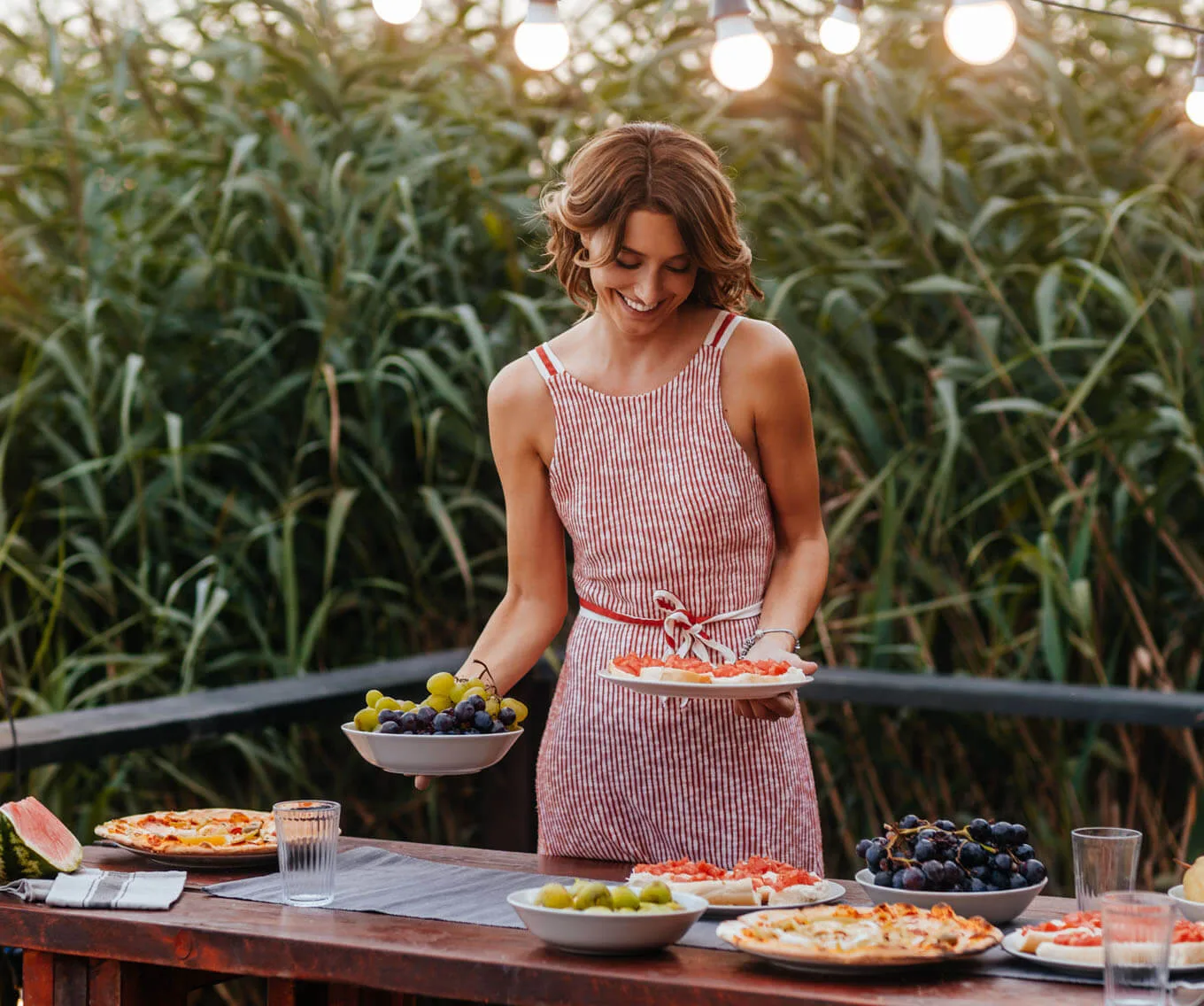 Woman preparing snacks for hosting a home outdoor gathering with string lights.