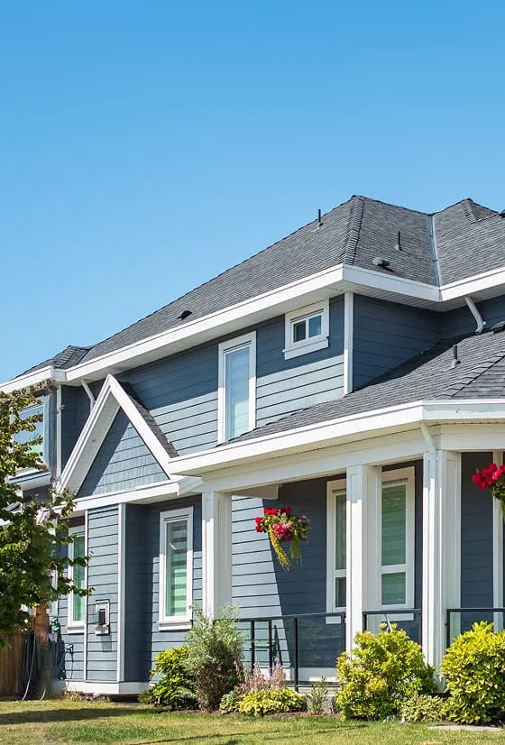 Blue two-story house with white trim, a gray roof, front porch, and colorful hanging flower baskets.