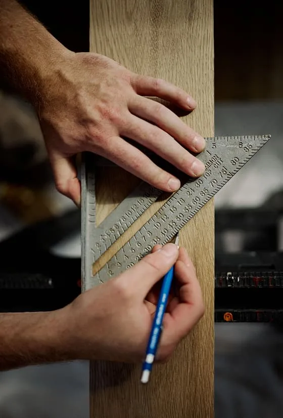 Person measuring a piece of wood with a ruler and marking it with a pencil.