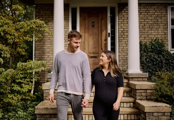 Young couple holding hands while walking in front of a home, representing today's first-time homebuyers.