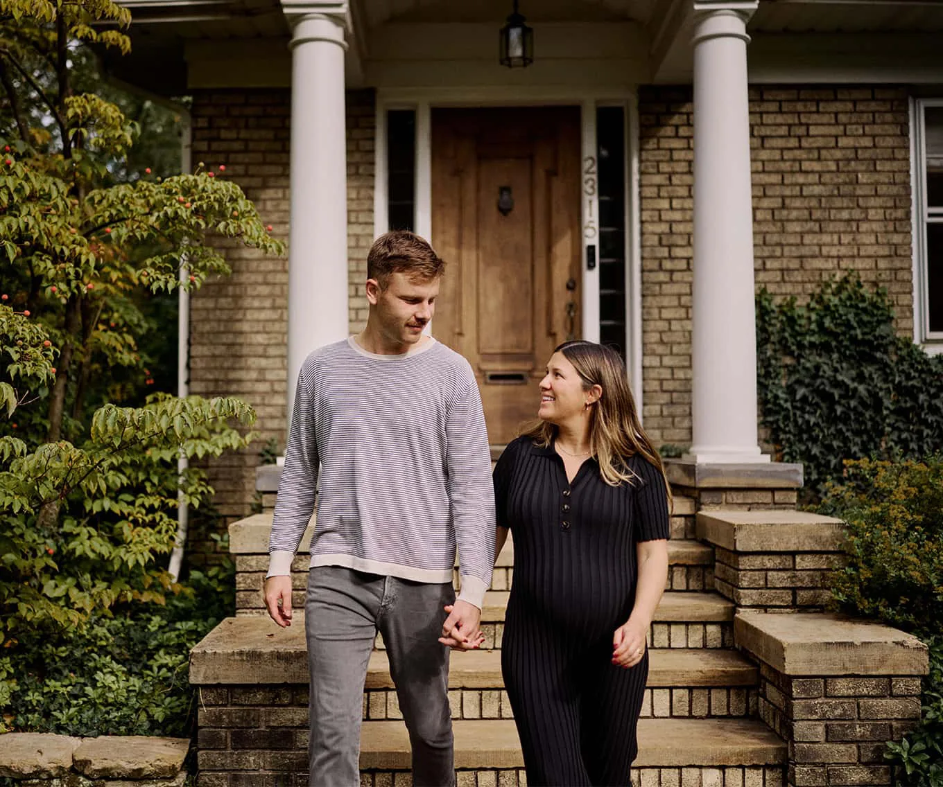 Young couple holding hands while walking in front of a home, representing today's first-time homebuyers.