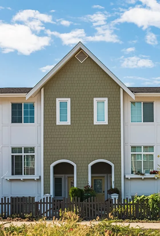 Exterior of a modern two-story townhome with green shingle siding, white trim, arched entryways and fenced front patios.