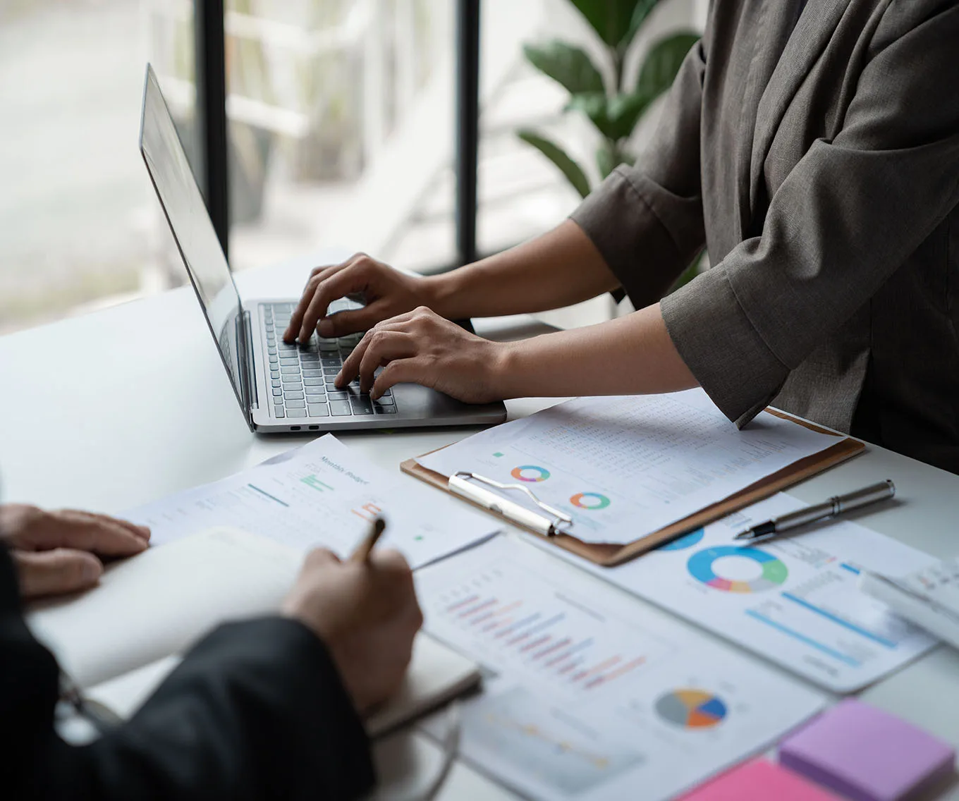 Two professionals collaborating at a desk with a laptop, charts, and financial report documents