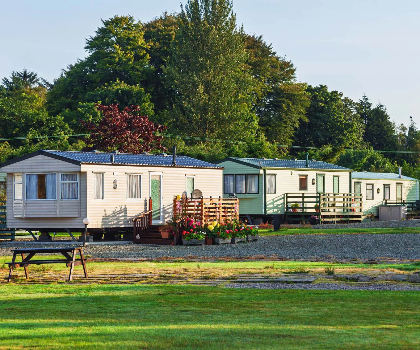 Three manufactured homes with porches beside a gravel lane, with grass and trees surrounding the community.