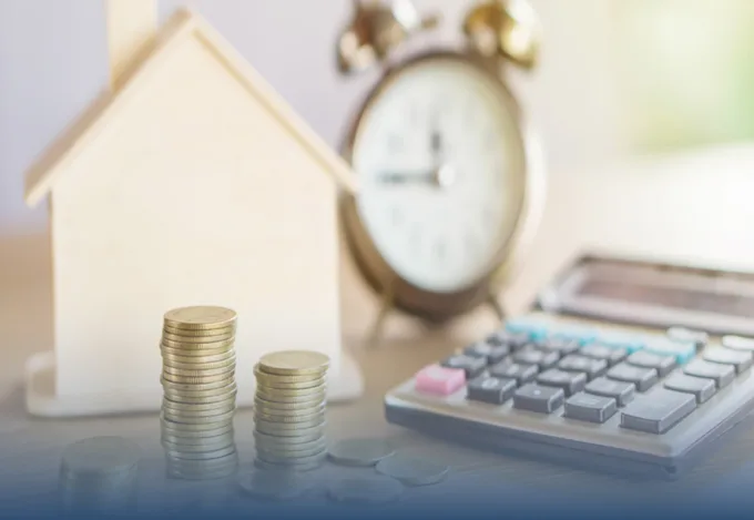 Stacked coins, a calculator, an alarm clock, and a wooden house model representing home financing and budgeting