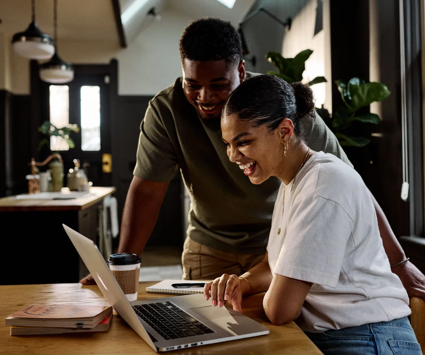 Two first-time homebuyers people smiling while looking at mortgage loans a laptop at a kitchen table.