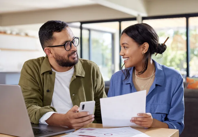 Couple reviewing financial documents together at a laptop while discussing credit scores and mortgage financing.